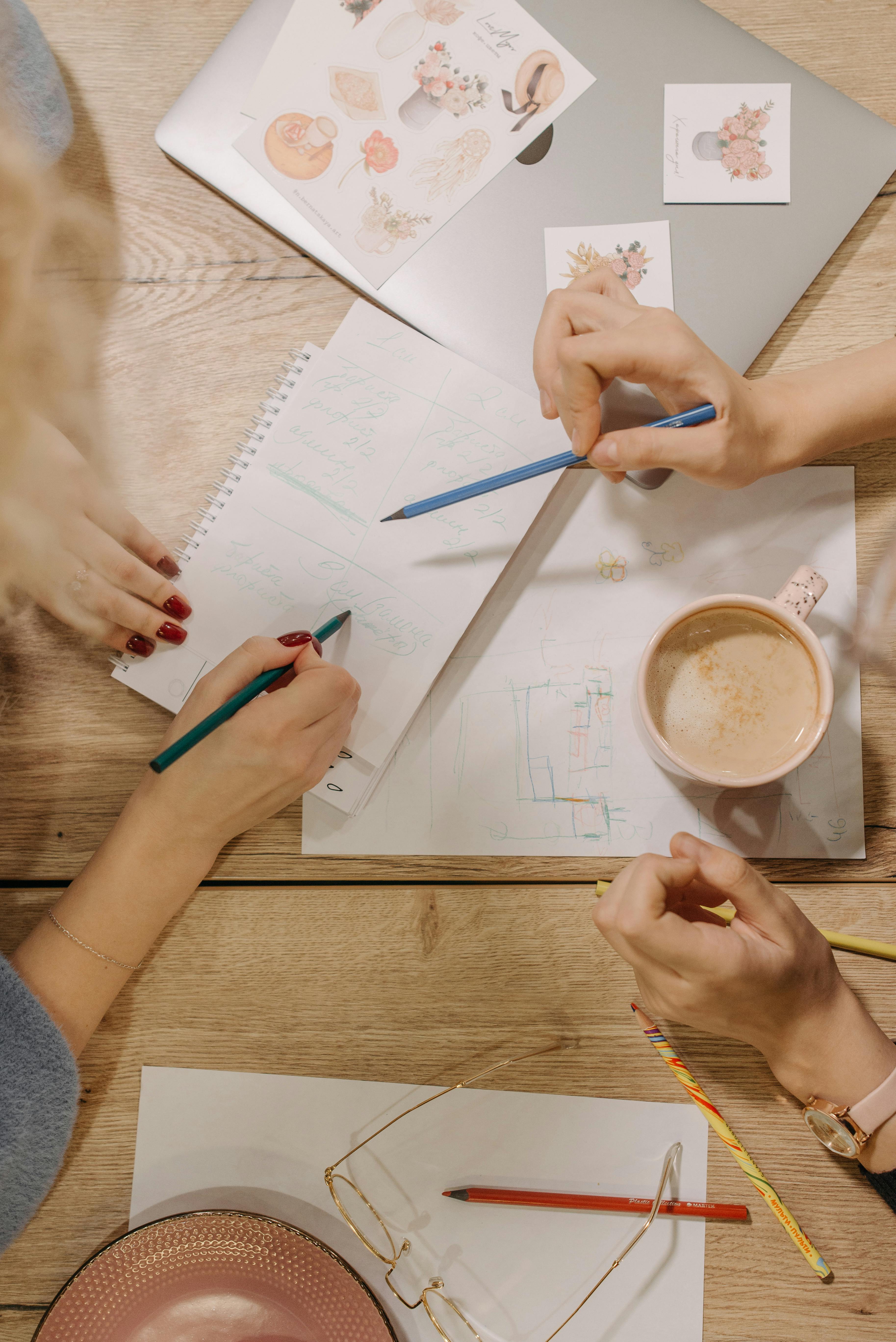 People Holding Pencils while Writing on White Paper