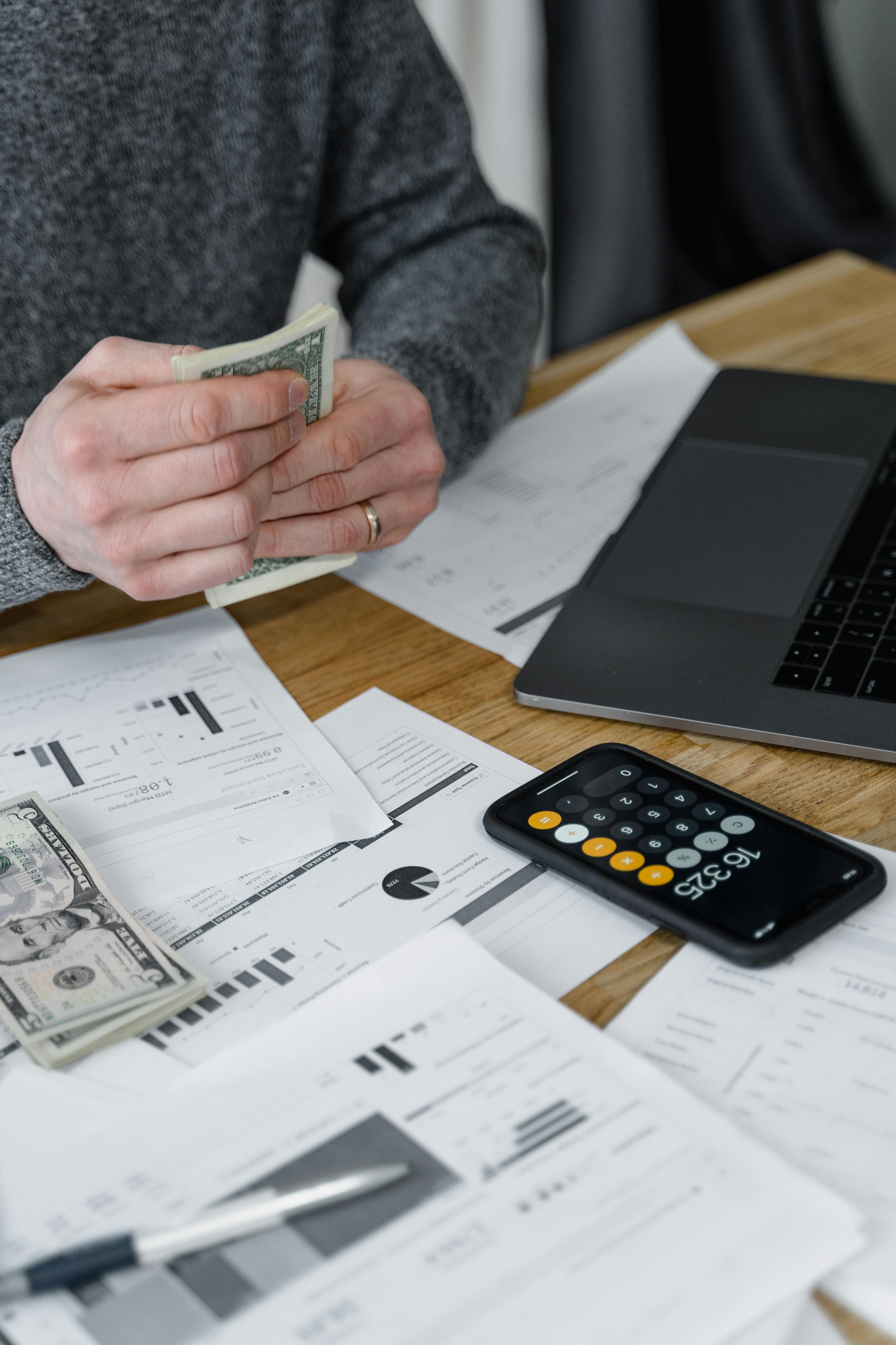man counting money with a calculator and business papers surround him